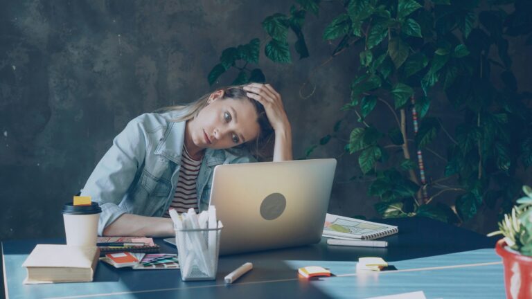 Workplace stress in working moms showing an overwhelmed mother working on a laptop in the office.