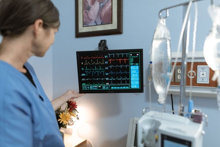 Nurse using clinical judgment in nursing to check ICU patient vitals on a bedside monitor.