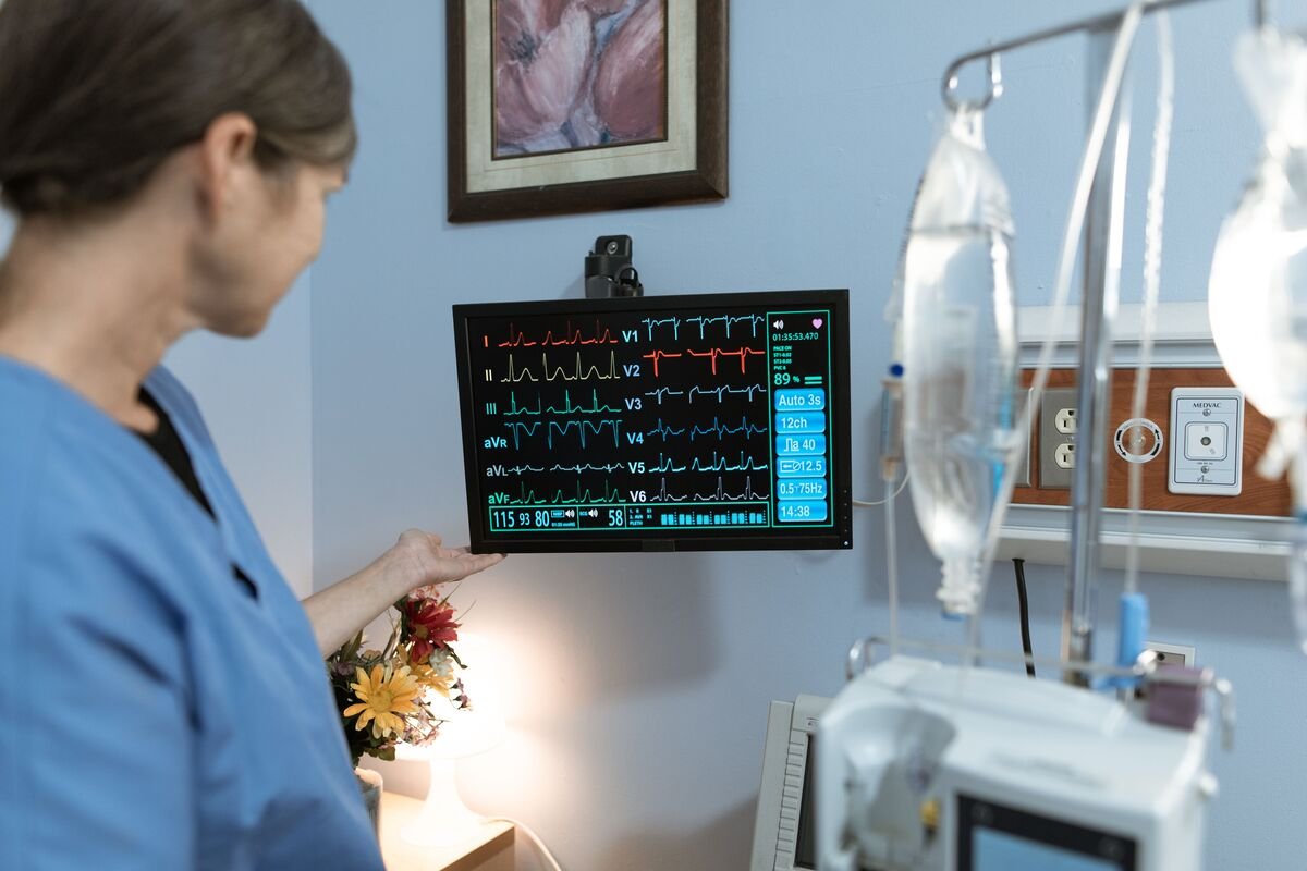 Nurse using clinical judgment in nursing to check ICU patient vitals on a bedside monitor.