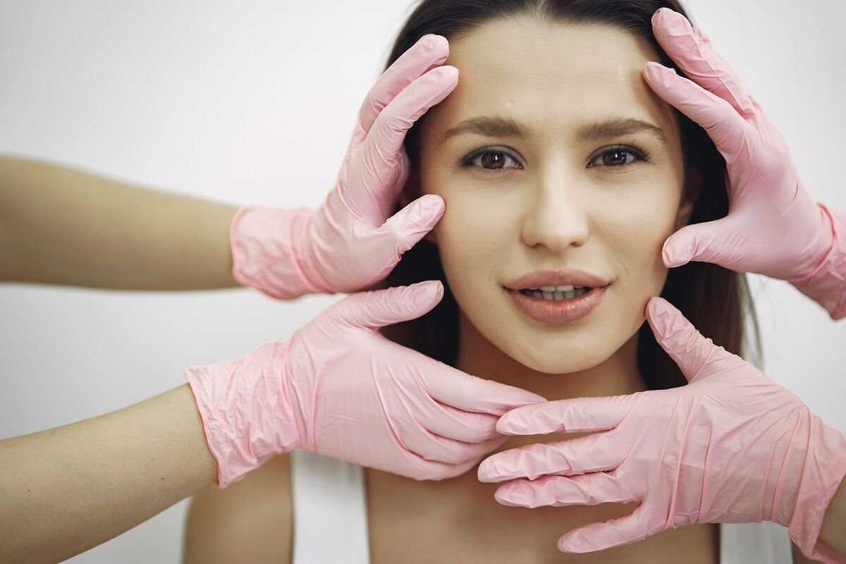 Skin and aesthetics gloved hands examining woman's clear facial skin