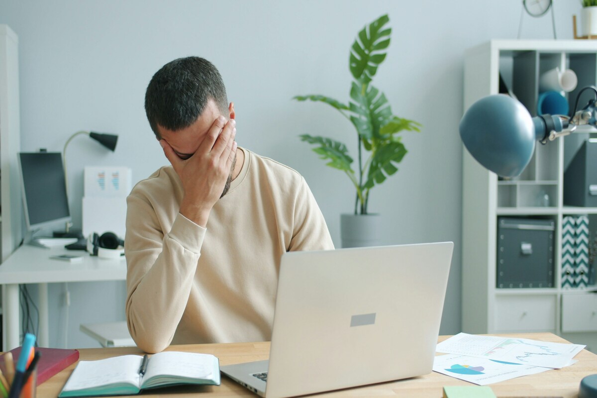 A stressed man sitting at an office desk looking overwhelmed, representing the stages of burnout.